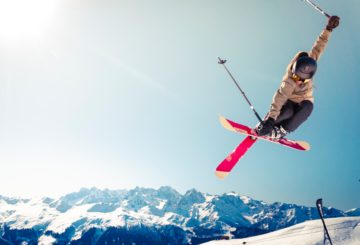 Skier in beige winter jacket doing a ski jump trick in the winter snowy mountains in beautiful weather