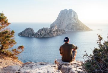 Man sits and watches and coastline and mountain