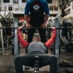 Six Pack Saturday - Man spotting another man in the gym while doing a bench press